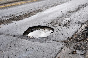 A large pot hole filled with water on an asphalt road